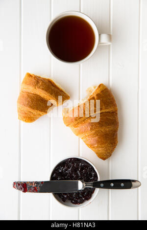 Gustosi croissant burroso, tazza di tè nero e marmellata in barattolo. Vista dall'alto. Foto Stock