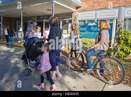 Merrick, New York, Stati Uniti d'America. Nov. 08, 2016. Il giorno delle elezioni, genitori, accompagnati dai loro figli sono al posto di polling in Park Avenue e la scuola elementare di votare per il Presidente e lo stato e i funzionari locali. A destra, una madre che ha votato in precedenza che giorno atteso per la sua moto per il marito e le figlie che hanno comprato cibo dal sesto grado allevatore nella scuola lobby. Foto Stock