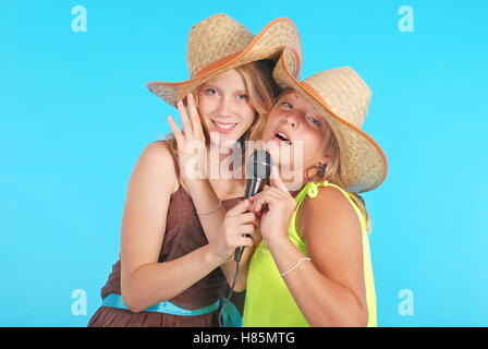 Due belle tredici anni di ragazze che indossano un grande paglia floppy cappello per il sole isolato su blu Foto Stock