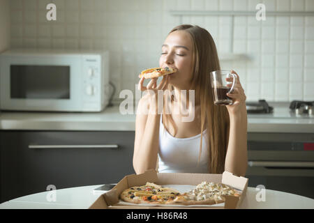 Ritratto di una giovane donna di mangiare la pizza in cucina Foto Stock