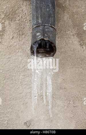 Il vecchio tubo di scarico con acqua congelata contro il muro Foto Stock
