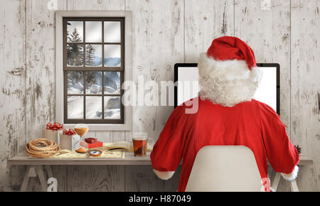 Babbo Natale lavoro sul computer nella sua stanza. Bianco parete in legno con finestra in background. Foto Stock