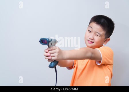 Asian boy scopo una pistola finta fatta con uno scanner di codici a barre, studio shot, sul muro grigio Sfondo con morbida ombra Foto Stock