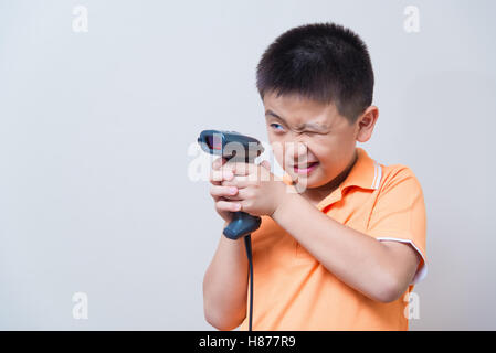 Asian boy scopo una pistola finta fatta con uno scanner di codici a barre, studio shot, sul muro grigio Sfondo con morbida ombra Foto Stock