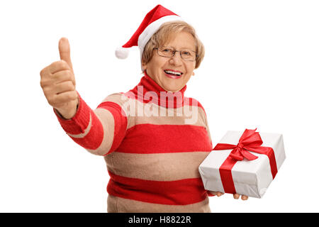 Allegro senior tenendo un regalo di natale e dando un pollice in alto isolato su sfondo bianco Foto Stock