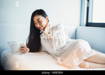 Una donna d'affari in preparazione per il lavoro, svegliarsi e controllando il suo smart phone nel letto. Foto Stock