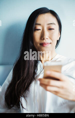 Una donna d'affari in preparazione per il lavoro, seduta a letto con il suo smart phone. Foto Stock