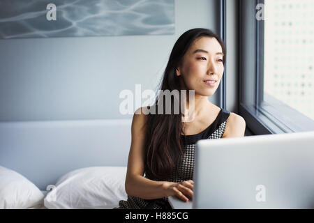 Un business donna vestita, seduta sul suo letto tramite un computer portatile. Foto Stock