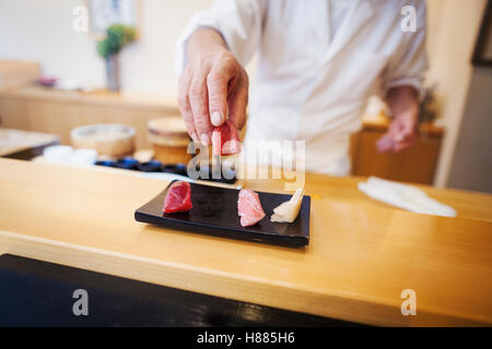 Uno chef che lavora in una piccola cucina commerciale, un itamae o master chef presentante una piastra fresca di sushi. Foto Stock