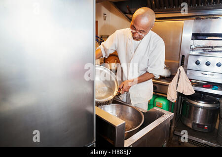 Uno chef che lavora in una piccola cucina commerciale, un itamae o master chef effettua il sushi. Preparare il riso per i piatti. Foto Stock