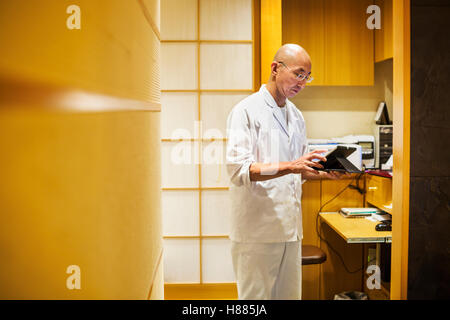 Lo chef in una piccola cucina commerciale, un itamae o master chef usando una tavoletta digitale. Foto Stock