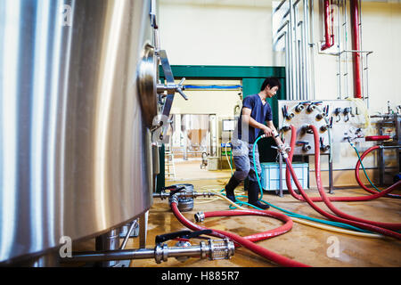 Uomo che lavora in una fabbrica di birra, tubi flessibili di collegamento a un metallo serbatoio di birra. Foto Stock