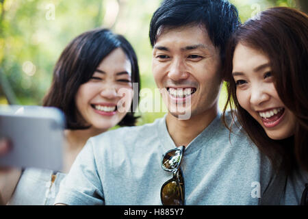 Due giovani donne e un uomo seduto in una foresta, prendendo un selfie. Foto Stock