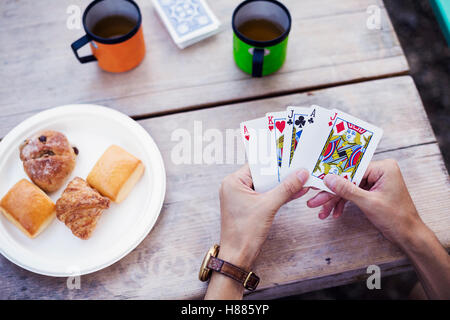 Close up di un uomo seduto a un tavolo, tenendo le carte da gioco. Foto Stock