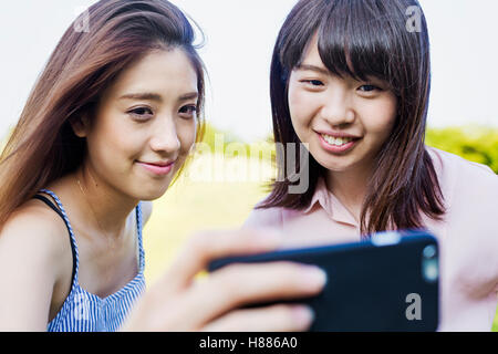Sorridente due giovani donne con capelli lunghi marrone, tenendo in mano un telefono cellulare, tenendo selfie. Foto Stock