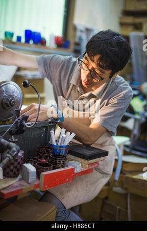 Un artigiano al lavoro in un vetro maker's workshop, utilizzando una macchina per attacco in vetro. Foto Stock
