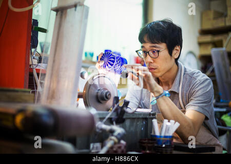 Un artigiano al lavoro in un produttore di vetro del workshop la lucidatura di un azzurro intenso cut oggetto in vetro. Foto Stock