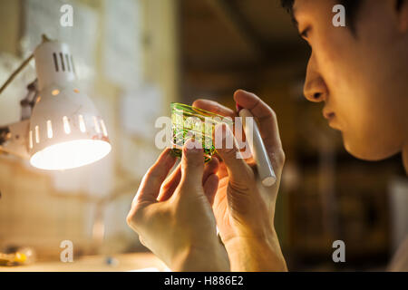 Un artigiano al lavoro in un vetro maker's studio workshop, ispezione di una piccola ciotola di vetro Foto Stock