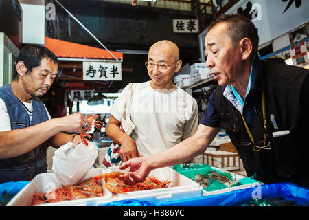 Mercato del pesce fresco in Tokyo. Due persone selezionando i crostacei per un cliente a comprare, riempimento di un sacco da box di gamberi. Foto Stock