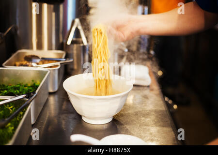 Un ramen noodle shop cucina. Uno chef che prepara le ciotole di spaghetti ramen in brodo, una specialità e fast food piatto. Foto Stock