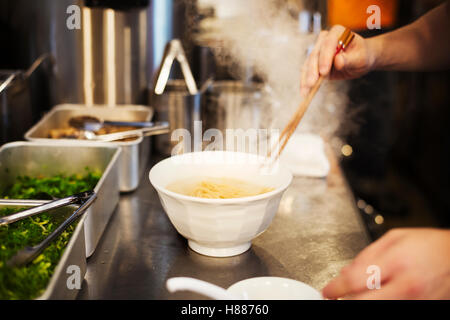 Un ramen noodle shop cucina. Uno chef che prepara le ciotole di spaghetti ramen in brodo, una specialità e fast food piatto. Foto Stock