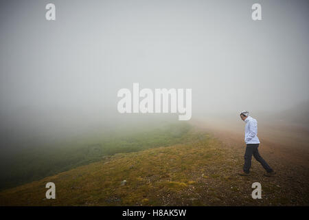 Donna cammina attraverso la nebbia nella tundra alpina Foto Stock
