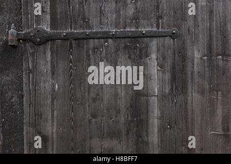 Cerniera e parte della porta di capannone costituito da vecchio verticale di tavole di legno con sbiaditi o nero vernice grigio Foto Stock