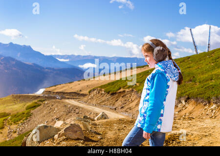 Ragazza con una spiralina, vestito in giacca sportiva e caldo auricolari morbidi, ammira di autunno paesaggio di montagna, Sochi, Russia Foto Stock