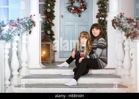 Mamma e figlia in casa accogliente, decorata entrata a casa con colori luminosi. La famiglia in attesa per il nuovo anno. Natale in famiglia Foto Stock