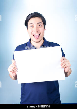 Asian uomo bello permanente e la mostra vuoto vuoto orizzontale carta in mani, , su sfondo blu. Foto Stock