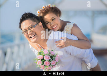 Ritratto di Allegro sposi abbracciando e guardando la telecamera. Asian sposi vicino al mare. Foto Stock