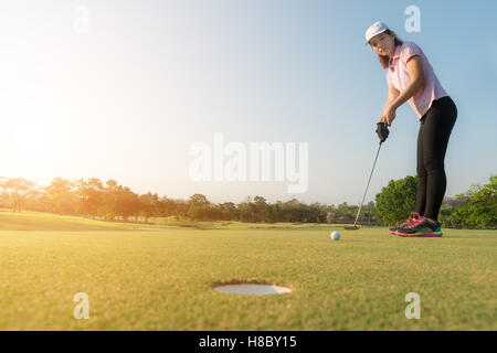 Donna asiatica giocatore di golf putting pallina da golf sul green, palla da golf cadere nel foro, cielo blu in background. Foto Stock