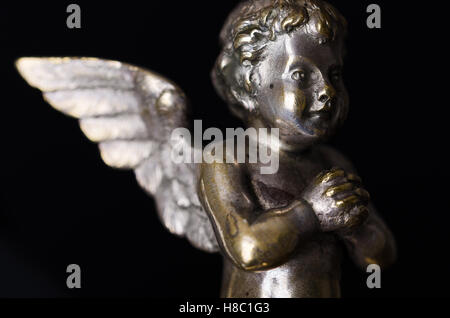 Pregando ottone angel vista laterale sul nero. Un putto alato di ottone ricoperta con argento, come parte di un candelabro. Foto Stock