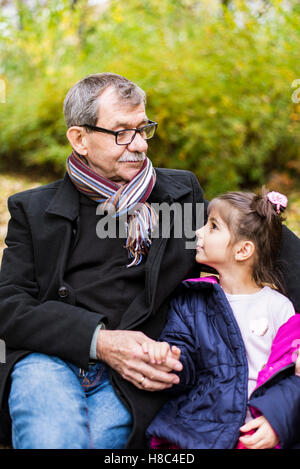 Bambina e nonno seduto su una panchina nel parco di autunno Foto Stock