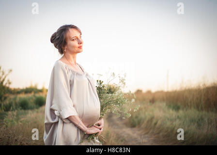 Ritratto di una giovane bella donna incinta sulla natura nella luce del tramonto. Foto Stock