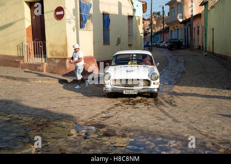 Un uomo cubano weari g un cappello da cowboy esce da un vecchio noi taxi nelle strade di ciottoli di Trinidad, Cuba Foto Stock