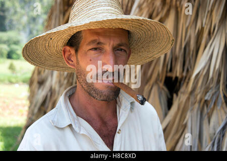 Ritratto di un agricoltore che indossa un cappello di paglia di fumare un sigaro con la paglia di essiccazione del tabacco casa sullo sfondo Vinales Cuba Foto Stock