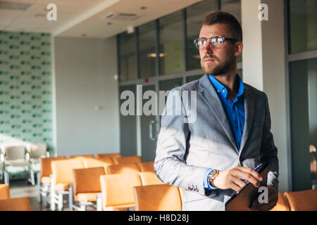 Imprenditore elegante in giacca e occhiali guarda fuori dalla finestra Foto Stock