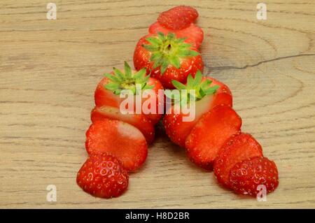 Il trio di fragole tagliate in strisce su una luce sullo sfondo di legno Foto Stock