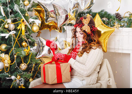 Ragazza carina spacchetta il dono ad albero di Natale. L'atmosfera di festa. Foto Stock