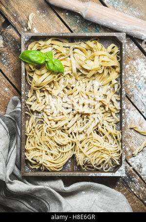 Vari fatti in casa non cotte fresche pasta italiana con la farina e il verde del basilico foglie nel vassoio di legno su sfondo squallido, vista dall'alto, Foto Stock