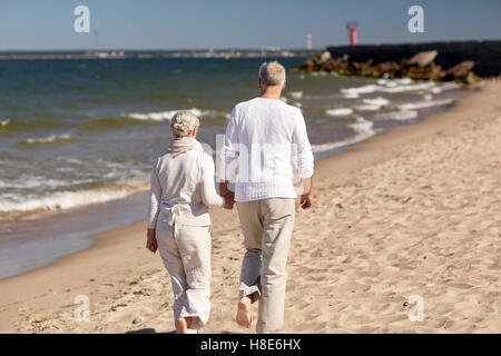 Coppia senior a piedi lungo la spiaggia di estate Foto Stock