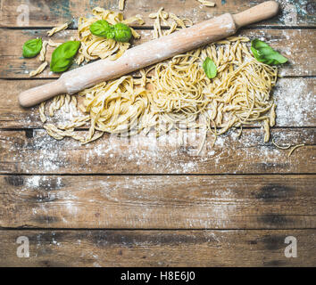 Vari fatti in casa non cotte fresche pasta italiana con la farina, il verde del basilico foglie e stantuffo sul malandato in legno rustico sfondo, top Foto Stock