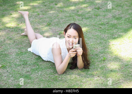 Ritratto di giovane donna giapponese posa su erba con lo smartphone Foto Stock