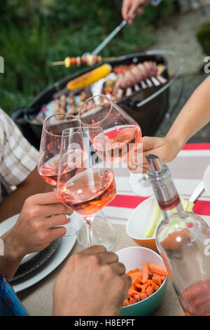 Happy amici avendo divertimento all'aperto, concentrarsi sulle mani la tostatura rose bicchiere di vino durante il barbecue Foto Stock