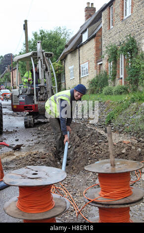 Un operaio installazione di cavi per superfast a banda larga in un territorio rurale Oxfordshire village, Regno Unito. Mostra i fusti di colore arancione del cavo ottico. Foto Stock