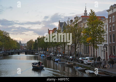 Una piccola barca che si muove in basso lungo uno di Amsterdam i tanti canali come set di sera. Foto Stock