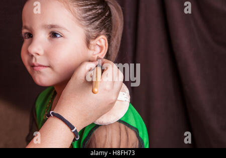 Poco carino ragazza rendendo facepaint prima festa di Halloween. Il make-up artist è di applicare alcuni foundation Foto Stock