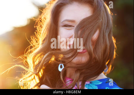 Felice giovane donna in posa il parco contro il tramonto Foto Stock