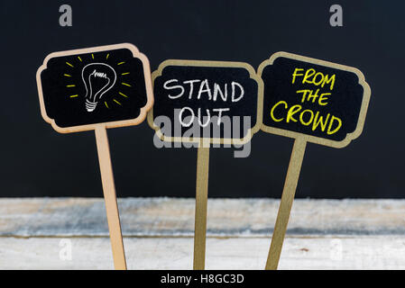 Messaggio di concetto di stare fuori dalla folla e lampadina della luce come simbolo per idea scritto con un gessetto su legno mini etichette di Blackboard Foto Stock